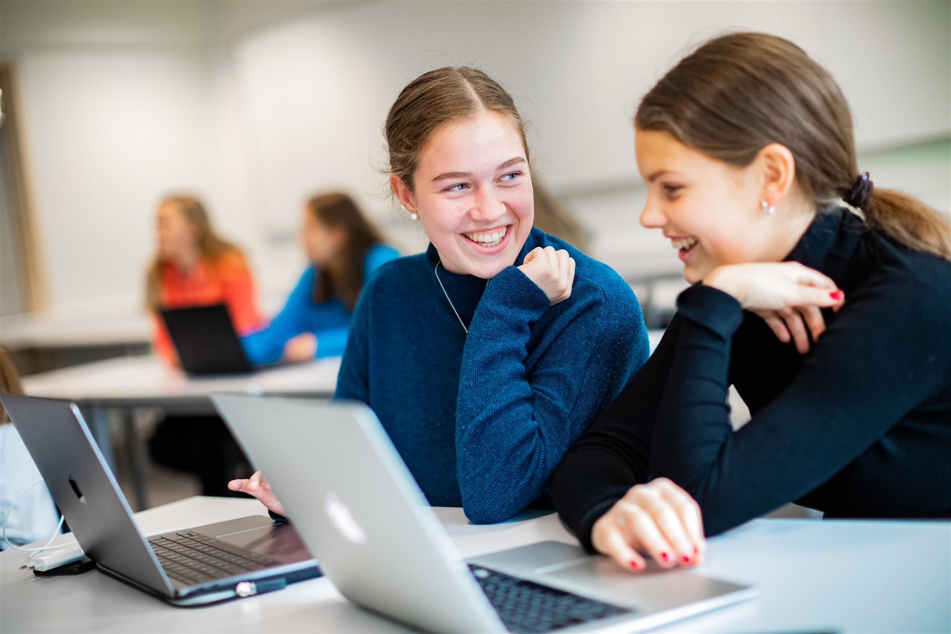 To jenter i blå genser sit med kvar sin pc i eit klasserom.