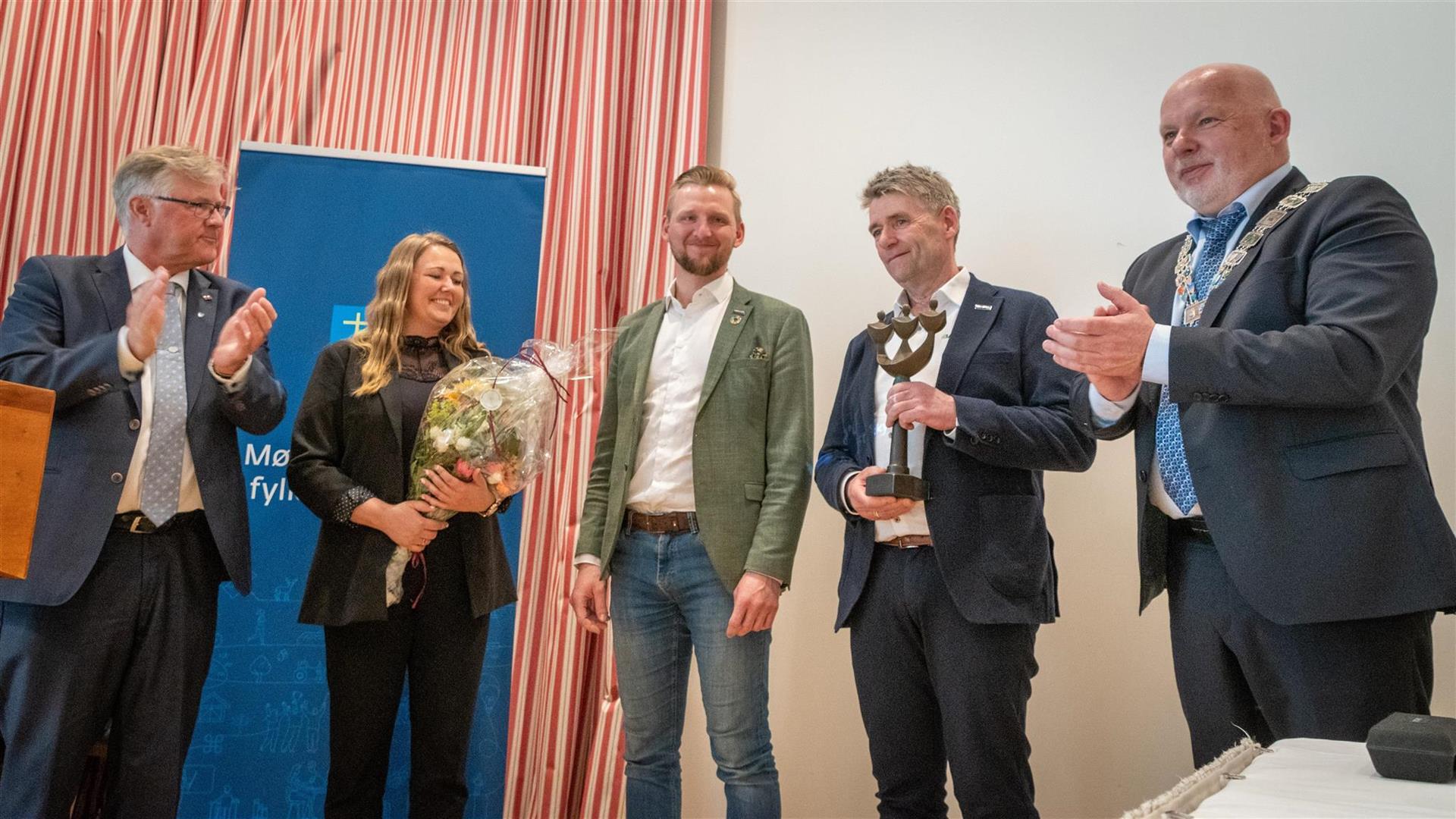 Fire menn i dress og kvinne i kjole som held blomar.