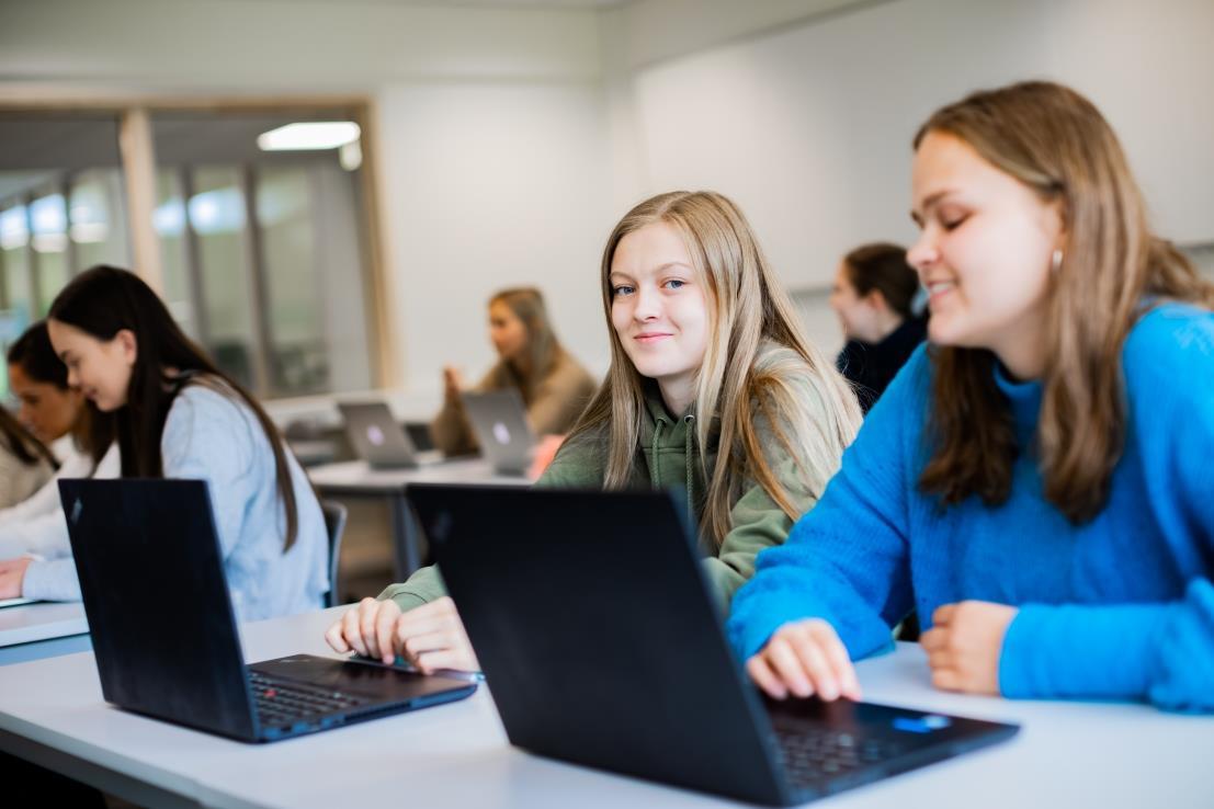 Jenter som sitt foran bærbare pc-ar, ser inn i kamera.